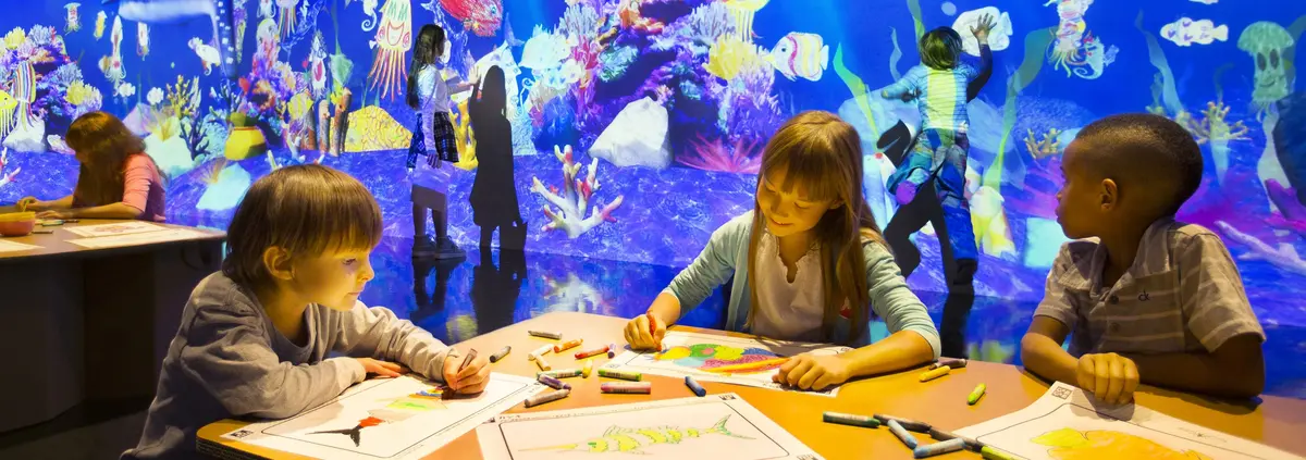 Drei Kinder zeichnen Fische vor einem digitalen Aquarium