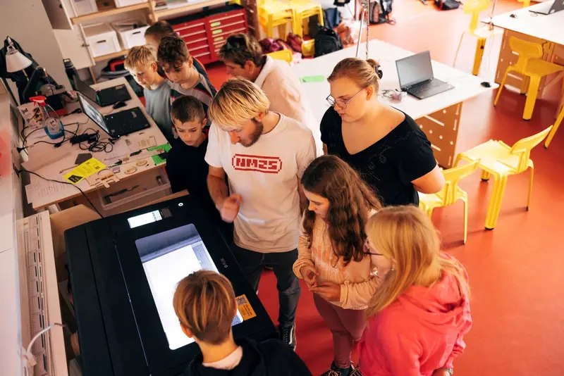 eine Gruppe junger Menschen steht um einen 3D-Drucker herum