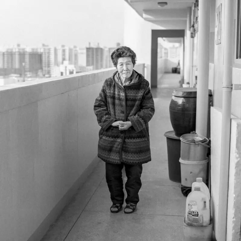 Foto einer älteren Frau auf einem Balkon eines Hochhauses