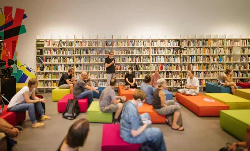 Menschen sitzen auf bunten Sitzkissen in einer Bibliothek