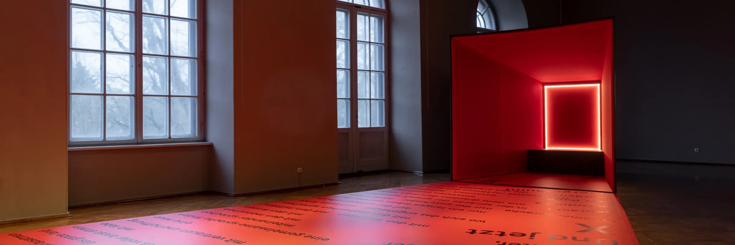 Ein Raum mit Fenstern und einer viereckigen, rot leuchtenden Kunstinstallation