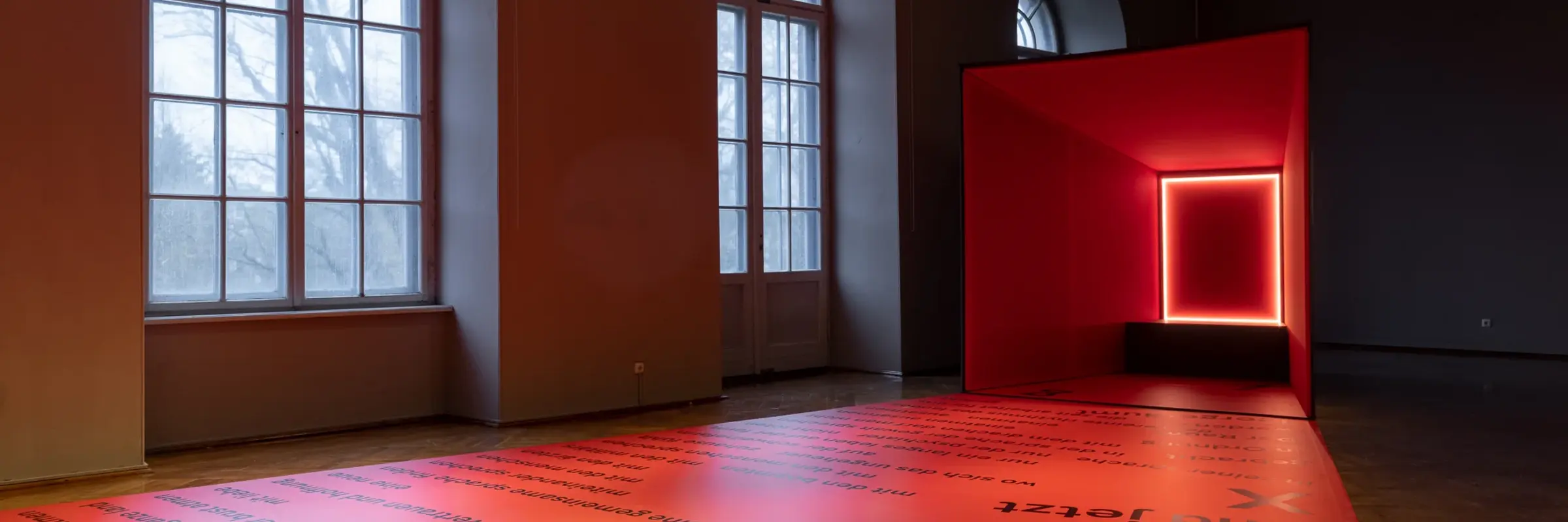 Ein Raum mit Fenstern und einer viereckigen, rot leuchtenden Kunstinstallation