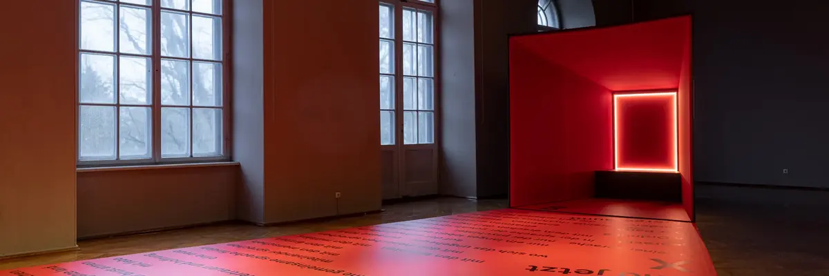 Ein Raum mit Fenstern und einer viereckigen, rot leuchtenden Kunstinstallation