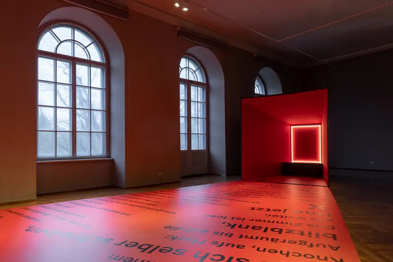 Ein Raum mit Fenstern und einer viereckigen, rot leuchtenden Kunstinstallation