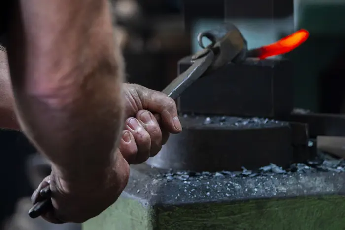 Hände, die mit einer Zange glühendes Metall bearbeiten 
